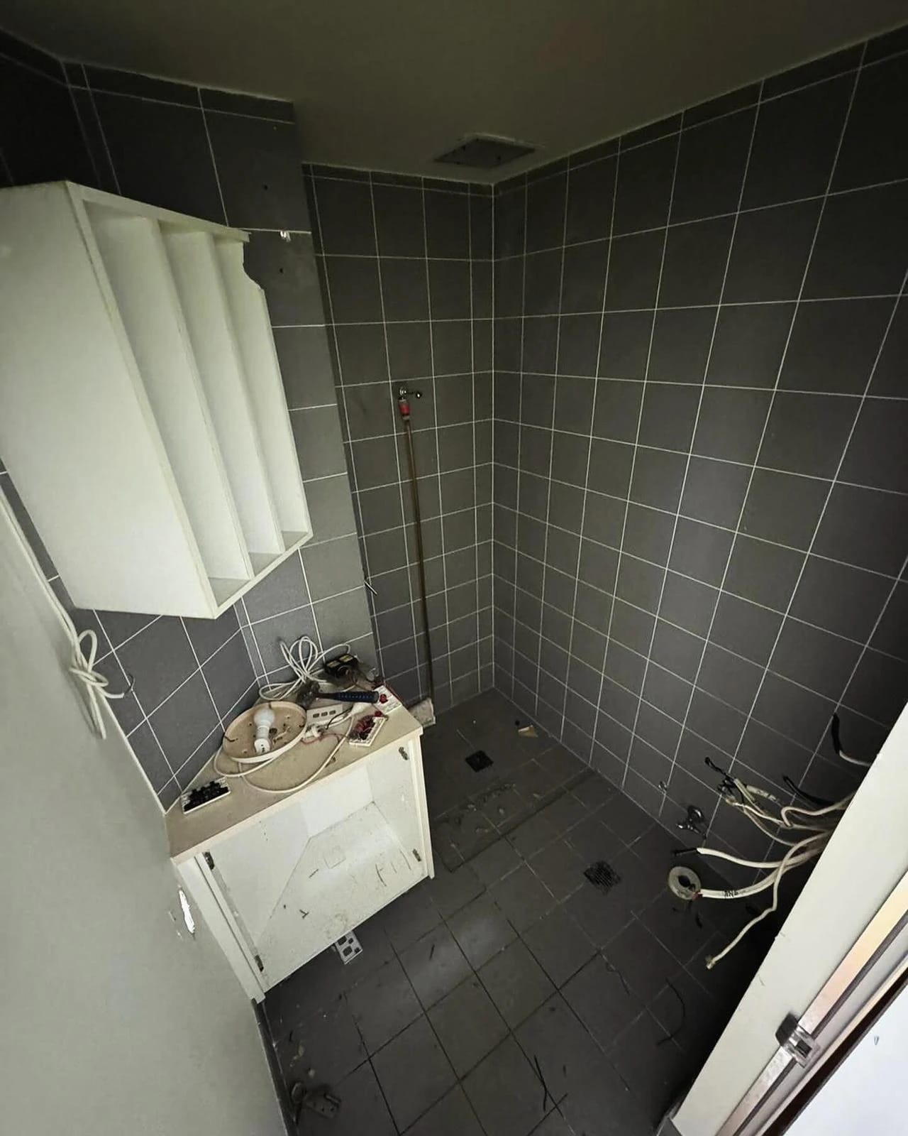 Dark-tiled bathroom with shower and vanity before strip out