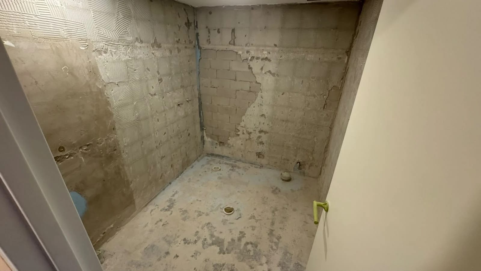 The same bathroom after fixtures and tiled finishes were removed, exposing masonry surfaces, floor substrate and retained service points