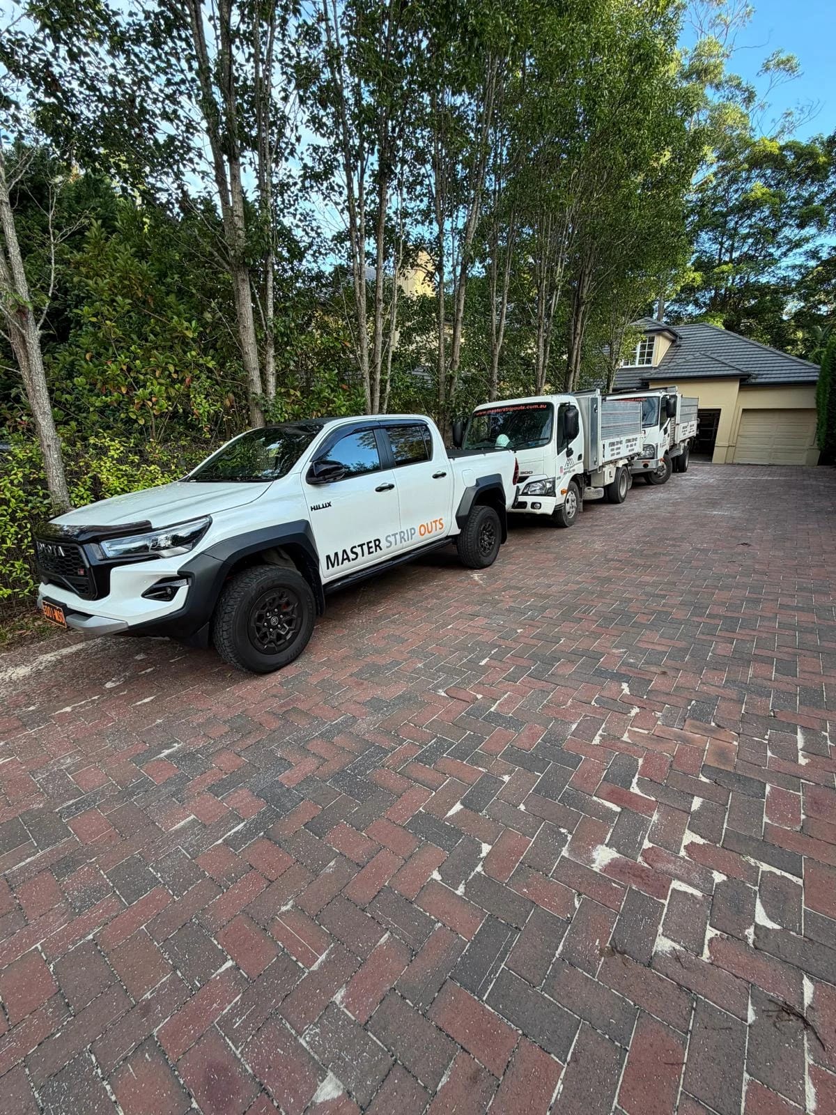 Master Strip Outs vehicles staged along the driveway at a residential demolition site