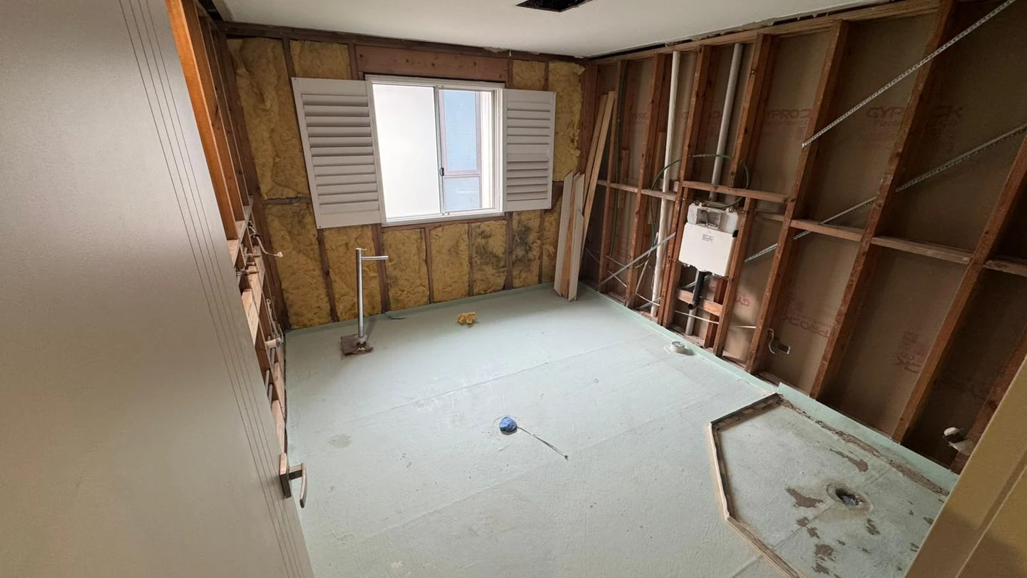 Stripped bathroom showing retained window, doorway, plumbing points and floor substrate