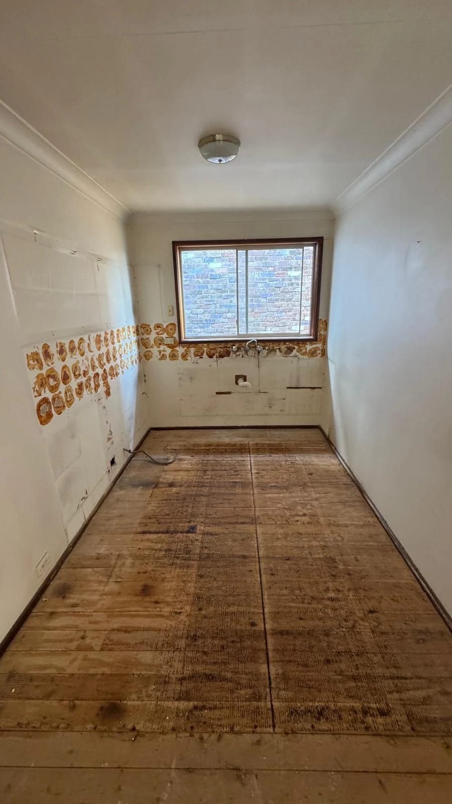 Galley kitchen after cabinets, appliances, splashback and floor finish were removed