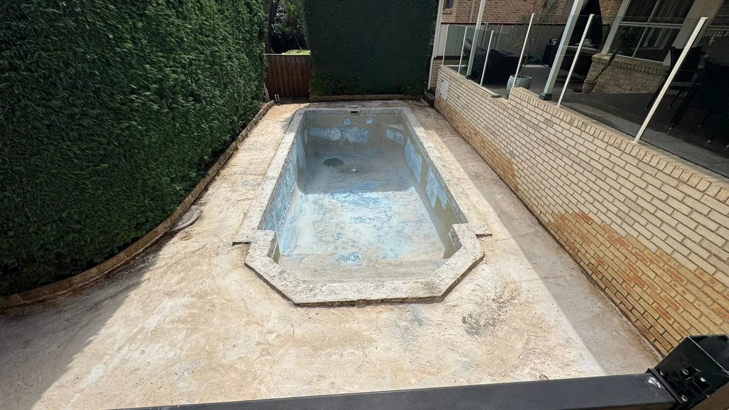 Compact backyard pool with the interior stripped and perimeter paving retained