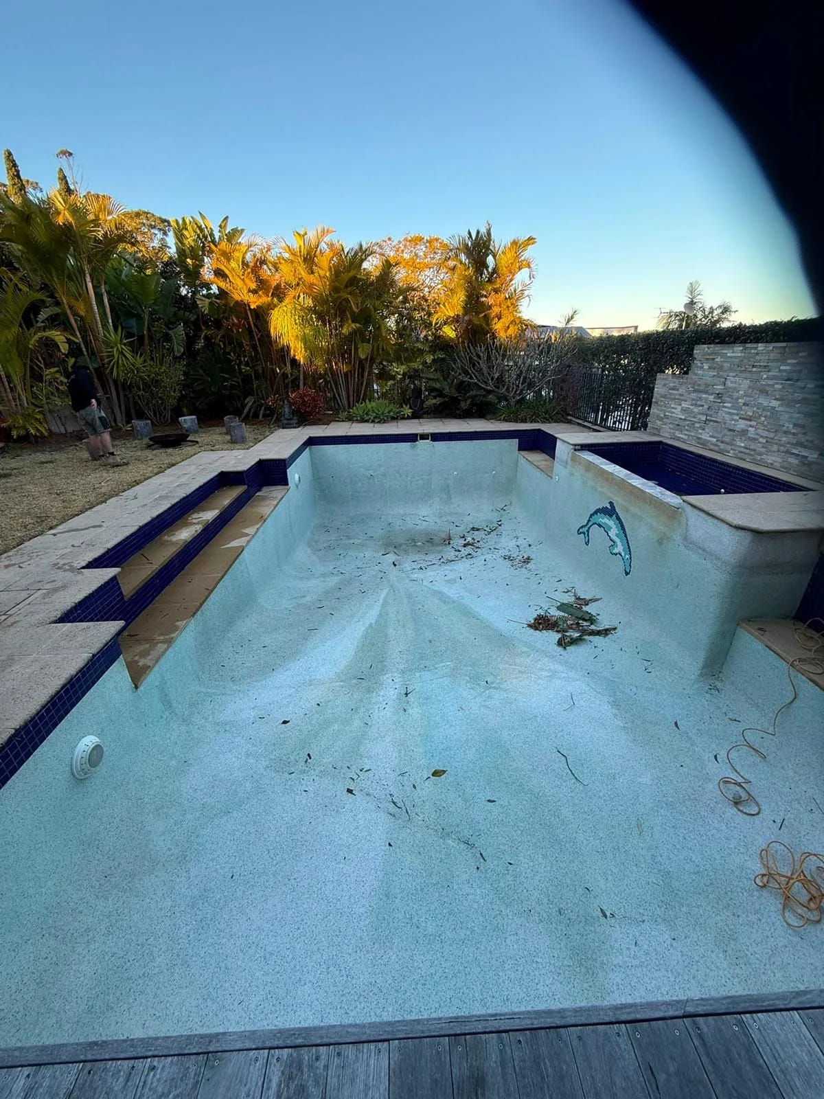 Drained residential pool and raised spa with the blue finish visible towards the garden before surface removal